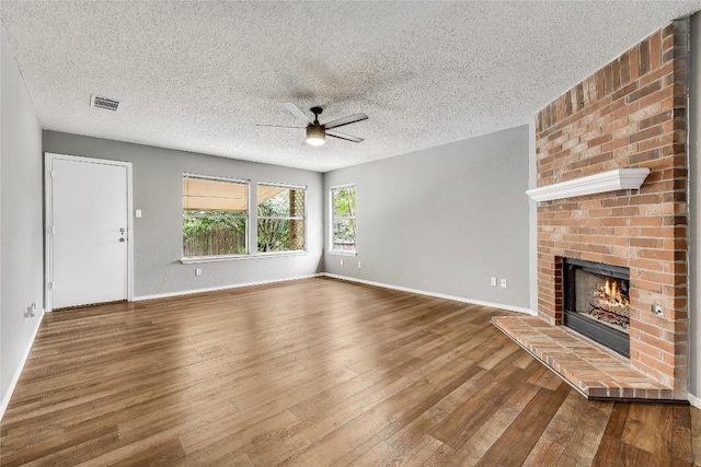 unfurnished living room featuring ceiling fan, a fireplace, wood finished floors, a textured ceiling, and baseboards