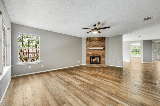 unfurnished living room with hardwood / wood-style flooring, ceiling fan, plenty of natural light, a textured ceiling, and a fireplace