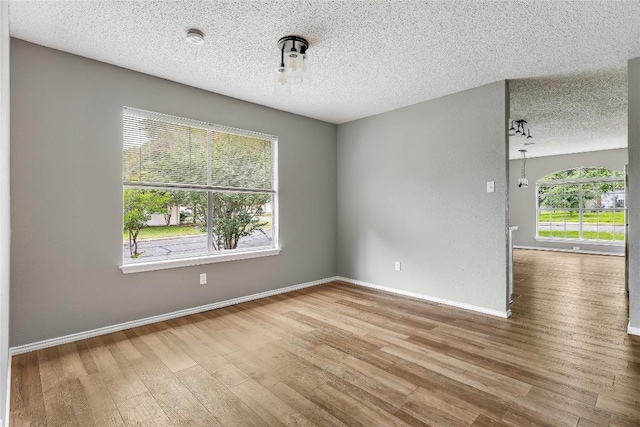 empty room with a textured ceiling, wood finished floors, and baseboards