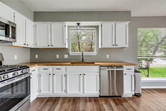 kitchen featuring stainless steel appliances, a sink, white cabinets, dark wood-style flooring, and a textured ceiling