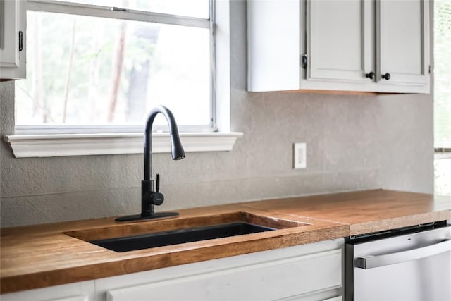 kitchen with dishwasher, a sink, decorative backsplash, wooden counters, and white cabinetry