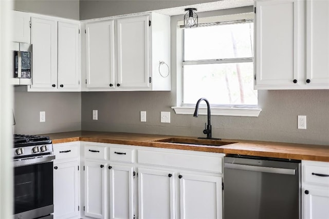 kitchen featuring wooden counters, stainless steel appliances, a sink, and white cabinetry