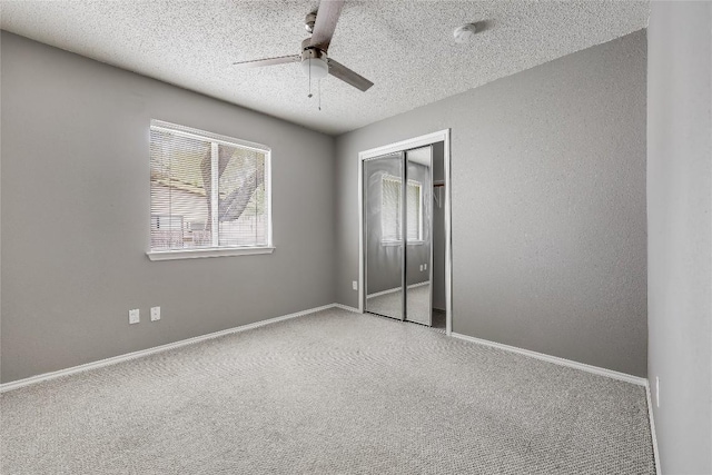 unfurnished bedroom with a textured ceiling, carpet floors, a closet, baseboards, and a ceiling fan