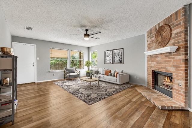 living area featuring ceiling fan, wood finished floors, a fireplace, baseboards, and a textured ceiling