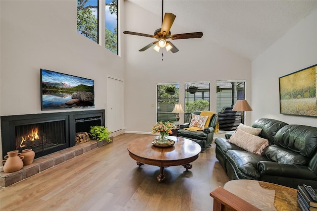 living room with high vaulted ceiling, ceiling fan, wood finished floors, a lit fireplace, and baseboards