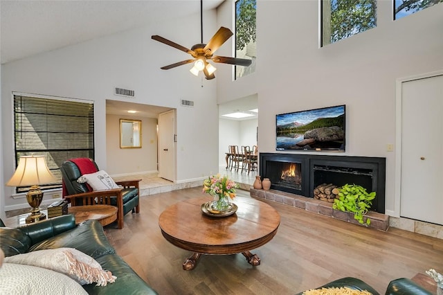 living room featuring high vaulted ceiling, wood finished floors, a ceiling fan, a warm lit fireplace, and baseboards
