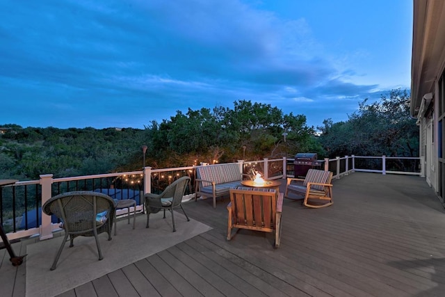 wooden terrace featuring an outdoor living space with a fire pit, a wooded view, and area for grilling