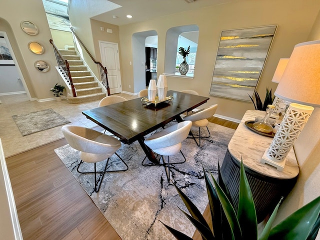 dining space with arched walkways, stairway, baseboards, wood finished floors, and recessed lighting