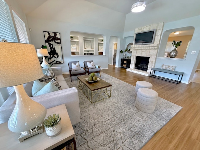 living area featuring arched walkways, wood finished floors, a fireplace, high vaulted ceiling, and baseboards