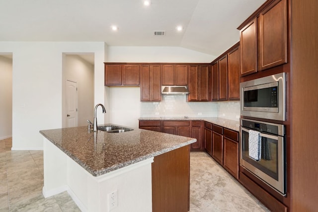kitchen featuring a sink, appliances with stainless steel finishes, decorative backsplash, dark stone countertops, and an island with sink