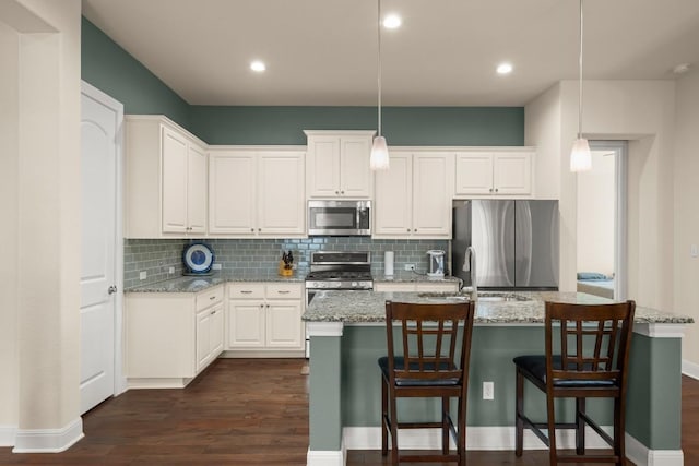 kitchen with appliances with stainless steel finishes, a sink, backsplash, dark wood-style floors, and white cabinetry