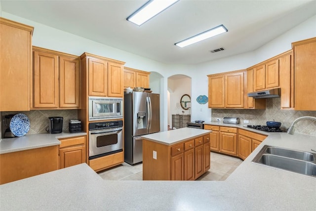 kitchen featuring appliances with stainless steel finishes, under cabinet range hood, a sink, arched walkways, and backsplash