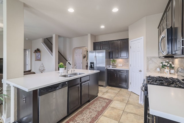 kitchen with stainless steel appliances, a sink, arched walkways, decorative backsplash, and light countertops