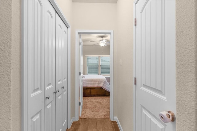 hallway featuring wood finished floors, a textured wall, and baseboards