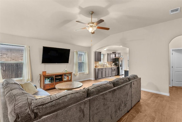 living area featuring arched walkways, ceiling fan, lofted ceiling, and baseboards