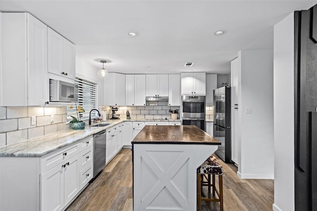 701 W Esparada Dr, Georgetown, TX 78628 - kitchen with stainless steel appliances, decorative backsplash, a sink, light wood-style flooring, and white cabinets