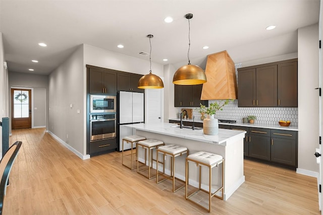 324 Pisa Ln, Georgetown, TX 78628 - kitchen with appliances with stainless steel finishes, decorative backsplash, light wood-type flooring, custom exhaust hood, and baseboards