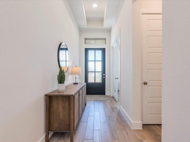 doorway featuring light wood-style flooring, a raised ceiling, baseboards, and a textured wall