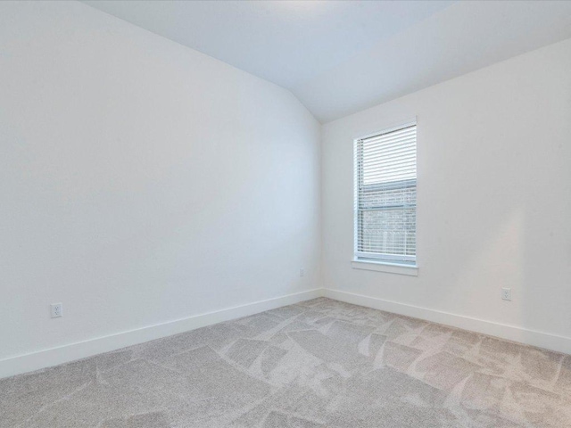 unfurnished room featuring vaulted ceiling, light colored carpet, and baseboards