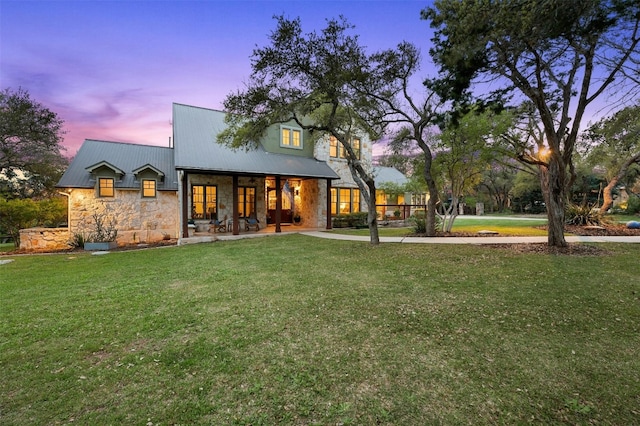 12316 Triple Creek Dr, Dripping Springs, TX 78620 - back of property at dusk with stone siding, a lawn, and metal roof