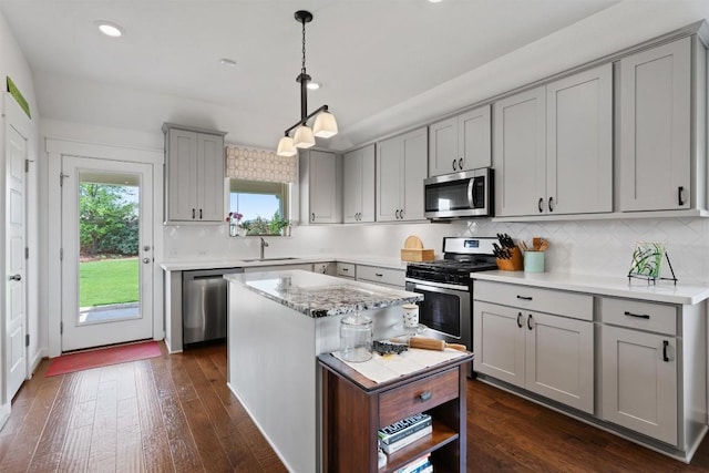 kitchen featuring appliances with stainless steel finishes, gray cabinetry, a kitchen island, dark wood-style floors, and a sink