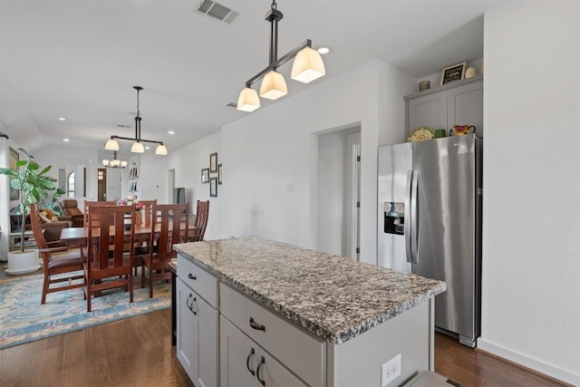 kitchen with stainless steel fridge with ice dispenser, a kitchen island, dark wood finished floors, decorative light fixtures, and light stone countertops