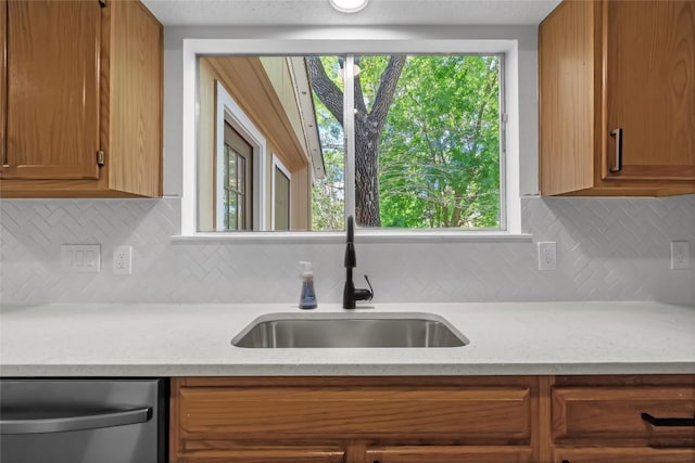 8800 Dandelion Trl, Austin, TX 78745 - kitchen featuring a sink, stainless steel dishwasher, decorative backsplash, brown cabinets, and light stone countertops