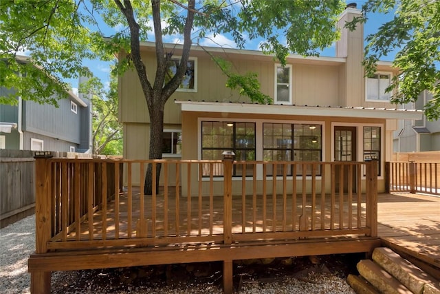 rear view of house with a deck, a chimney, and fence