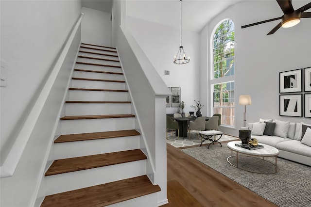 staircase with wood finished floors, high vaulted ceiling, a ceiling fan, and a chandelier
