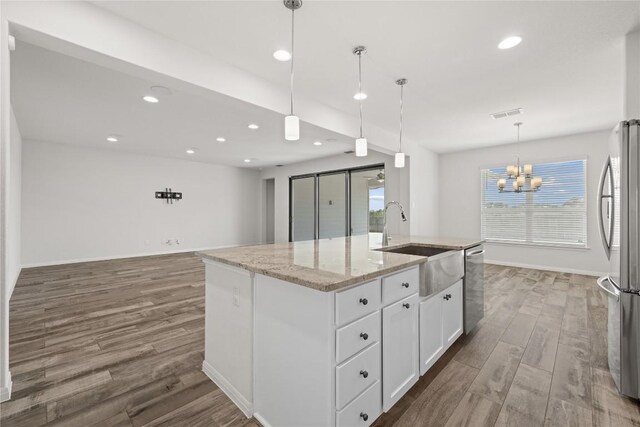 5213 Fresno Ave, Pflugerville, TX 78660 - kitchen with stainless steel appliances, wood finished floors, a chandelier, white cabinets, and light stone counters