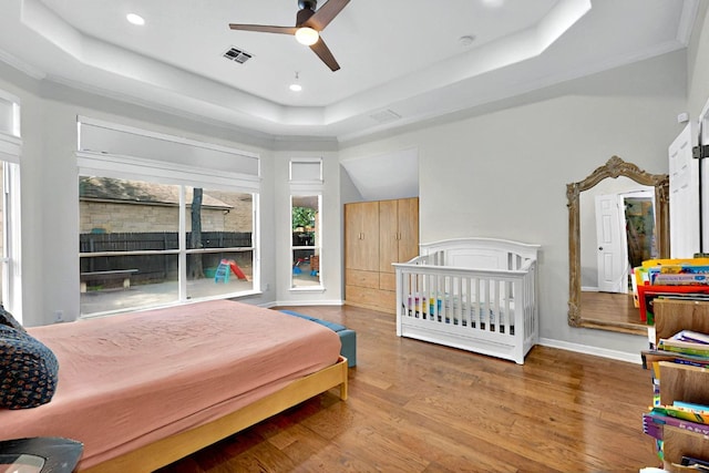 bedroom with a raised ceiling, wood finished floors, recessed lighting, ceiling fan, and baseboards
