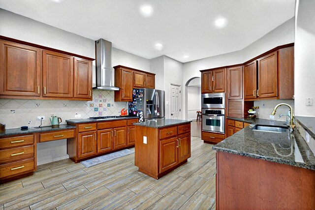 kitchen with appliances with stainless steel finishes, a sink, wall chimney range hood, dark stone countertops, and recessed lighting