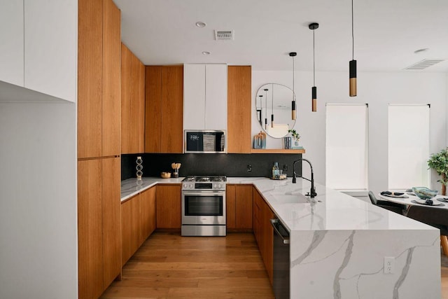 1140 Northwestern Ave Unit 2, Austin, TX 78702 - kitchen with appliances with stainless steel finishes, a peninsula, modern cabinets, light wood-type flooring, and light stone counters