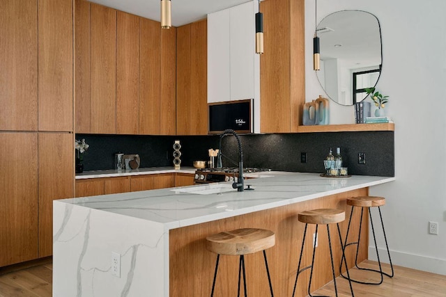 1140 Northwestern Ave Unit 2, Austin, TX 78702 - kitchen with modern cabinets, brown cabinetry, a peninsula, light stone counters, and backsplash