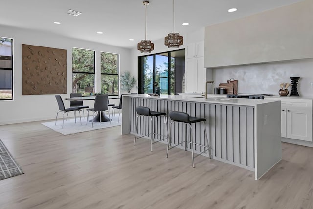 214 Ulupau Cir, Bastrop, TX 78602 - kitchen with light wood finished floors, white cabinets, recessed lighting, a center island with sink, and light countertops