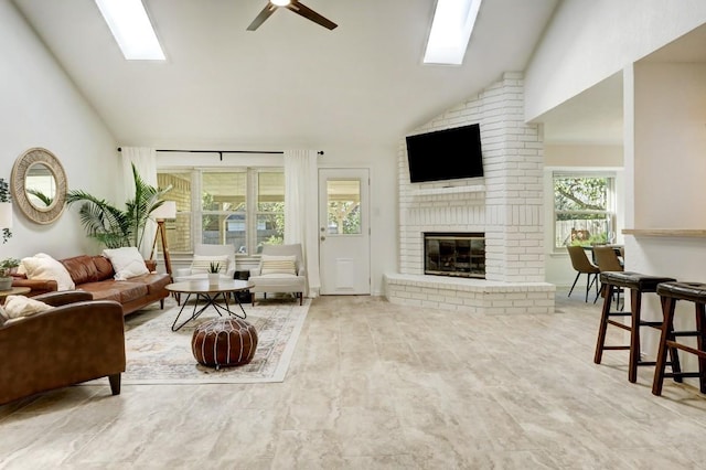 living room featuring a ceiling fan, a brick fireplace, a skylight, and high vaulted ceiling