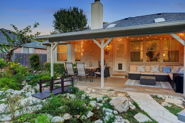 back of house at dusk featuring an outdoor living space, fence, a patio area, and a chimney