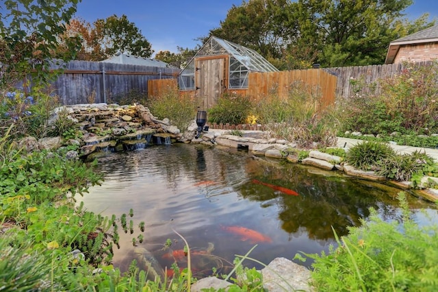 water view featuring fence, a garden pond, and a greenhouse