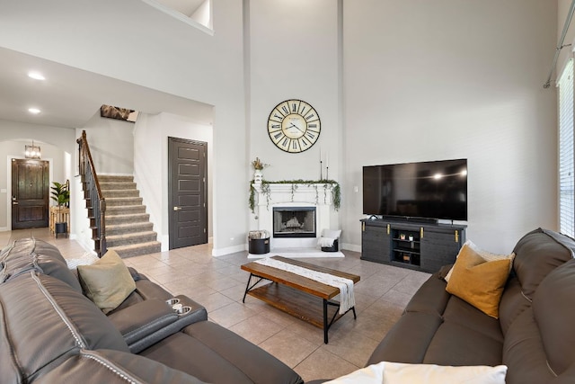 tiled living area featuring a towering ceiling, stairs, a fireplace with raised hearth, and baseboards