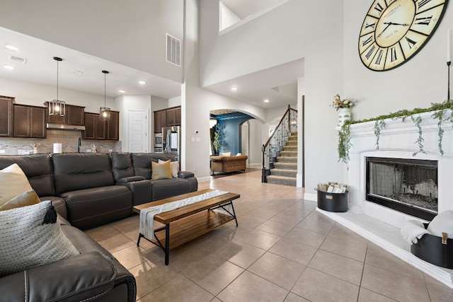 living area with arched walkways, a fireplace with raised hearth, baseboards, stairs, and a high ceiling
