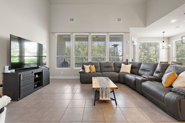 living area with light tile patterned floors, a towering ceiling, a chandelier, and baseboards