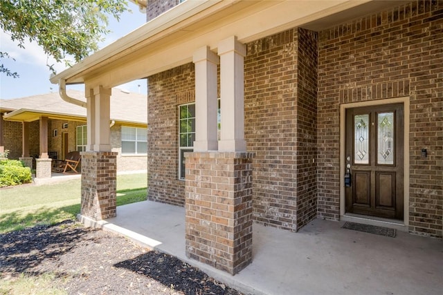 view of exterior entry with brick siding and covered porch