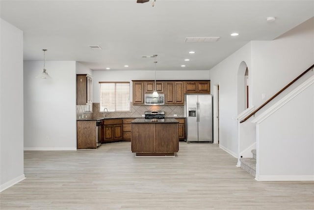 kitchen featuring stainless steel appliances, light wood finished floors, dark countertops, a center island, and recessed lighting