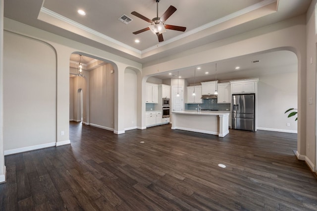 19817 Chayton Cir, Pflugerville, TX 78660 - unfurnished living room featuring a tray ceiling, arched walkways, a ceiling fan, crown molding, and dark wood-style floors
