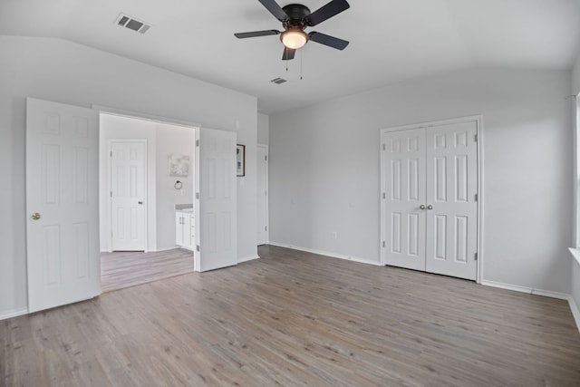 unfurnished bedroom with lofted ceiling, wood finished floors, baseboards, a ceiling fan, and a closet