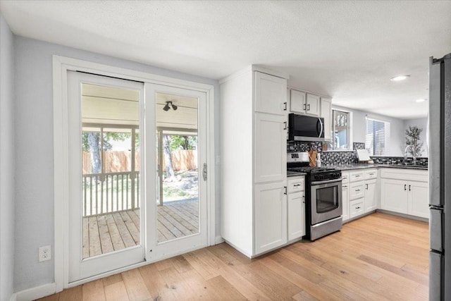 kitchen with stainless steel appliances, light wood-type flooring, white cabinets, tasteful backsplash, and a sink