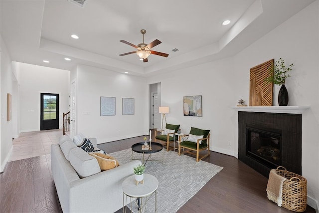 living room with a raised ceiling, recessed lighting, a glass covered fireplace, baseboards, and a ceiling fan