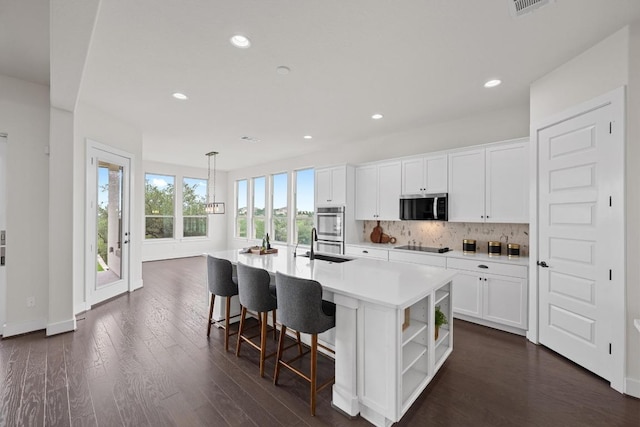 kitchen with appliances with stainless steel finishes, open shelves, white cabinets, tasteful backsplash, and a kitchen island with sink
