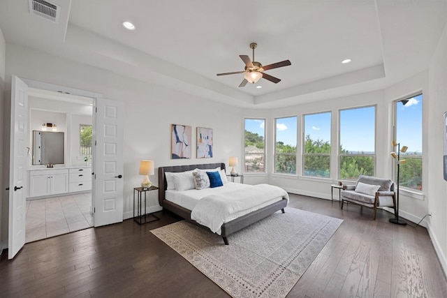 bedroom with a tray ceiling, dark wood-style floors, baseboards, recessed lighting, and connected bathroom
