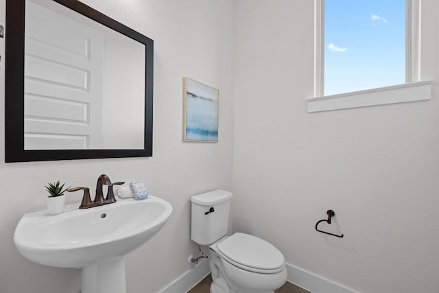 half bath with baseboards, toilet, and a sink